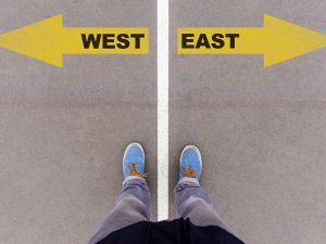 West and East text arrows on asphalt ground, feet and shoes on f
